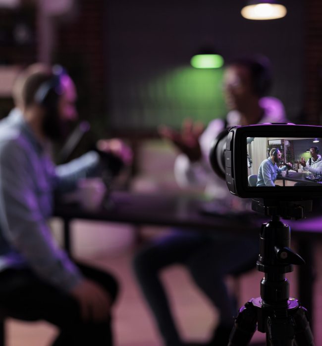 Multiethnic team of people meeting to broadcast internet podcast, recording video discussion on camera. Influencer and guest talking on online livestream to create social media channel content.